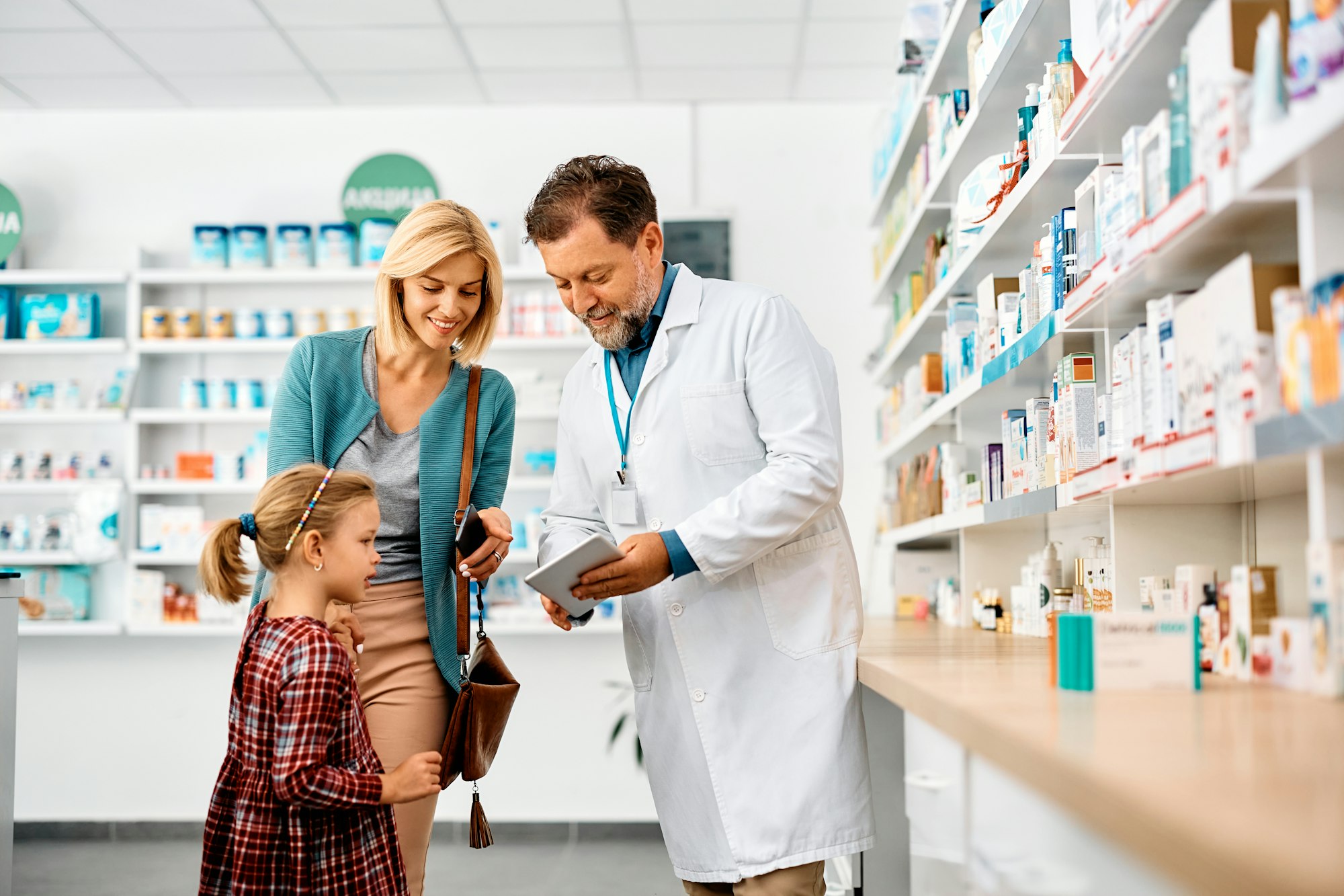 Happy mother and daughter using touchpad with their pharmacist in a pharmacy,